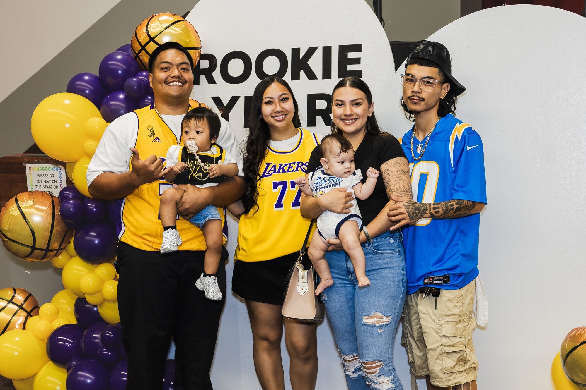 Families pose with babies at a basketball-themed first-birthday party with a balloon arch in Hawaii